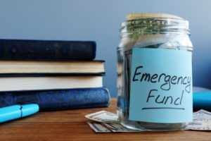 A jar of money labeled emergency funds sits on a table.