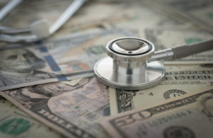 A stethoscope rests on top of a money pile.