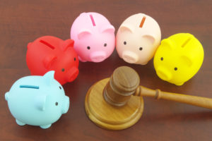 Several piggy banks surround a wooden gavel on a table.