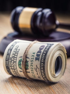 A bundle of money tied with string in front of a gavel.
