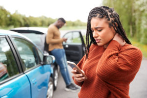 woman holding her neck and texting after a car accident