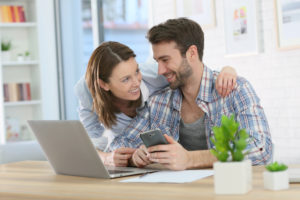 couple at home using smartphone and laptop to pay bills